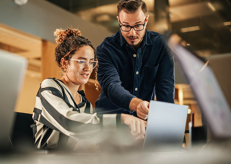 Two Colleagues Working On Laptop in Office as they Discuss a Project